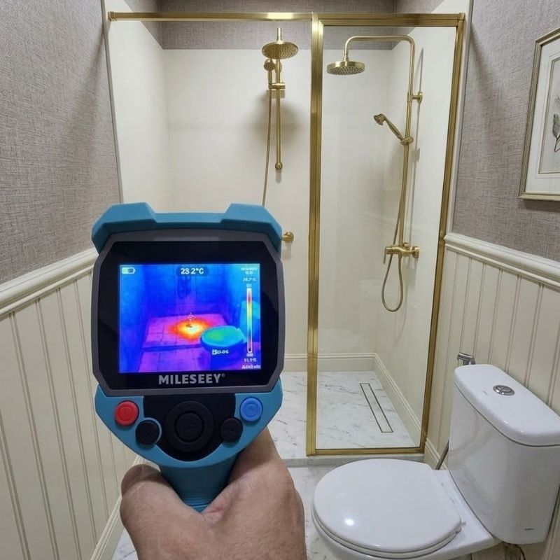 Handheld thermal imaging device checking shower leak detection in modern bathroom